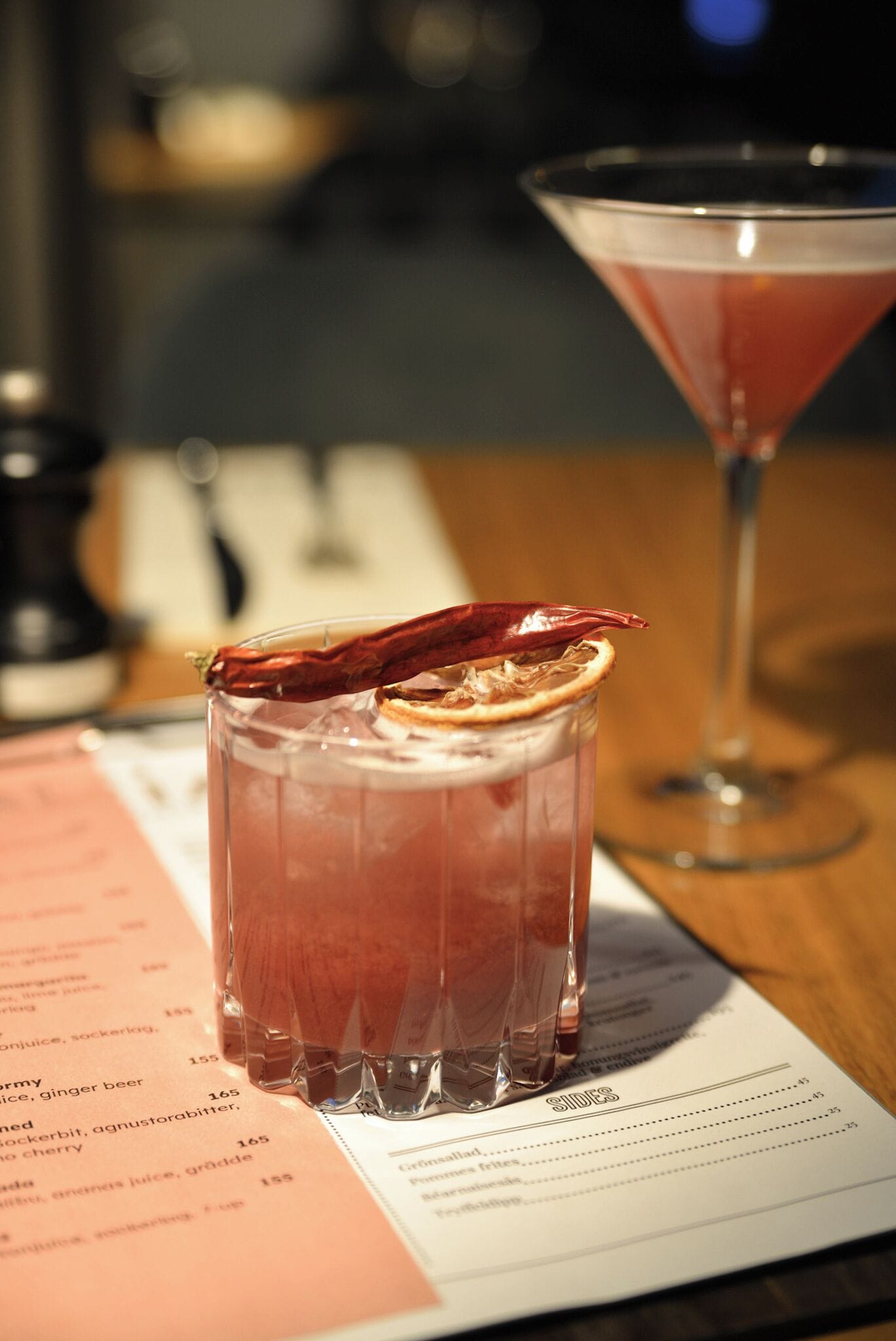A menu with a glass of red drink garnished with a dried orange slice and a red chili pepper.