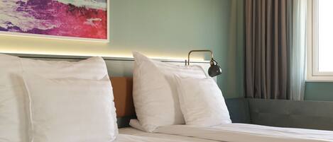 A neatly made bed with white linens, a headboard, and a bedside lamp.