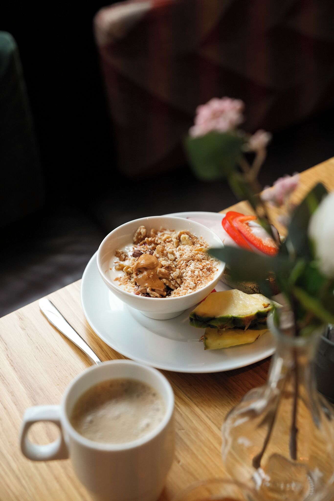 A breakfast setting with a bowl of cereal, a slice of tomato, and a glass of coffee on a wooden table.