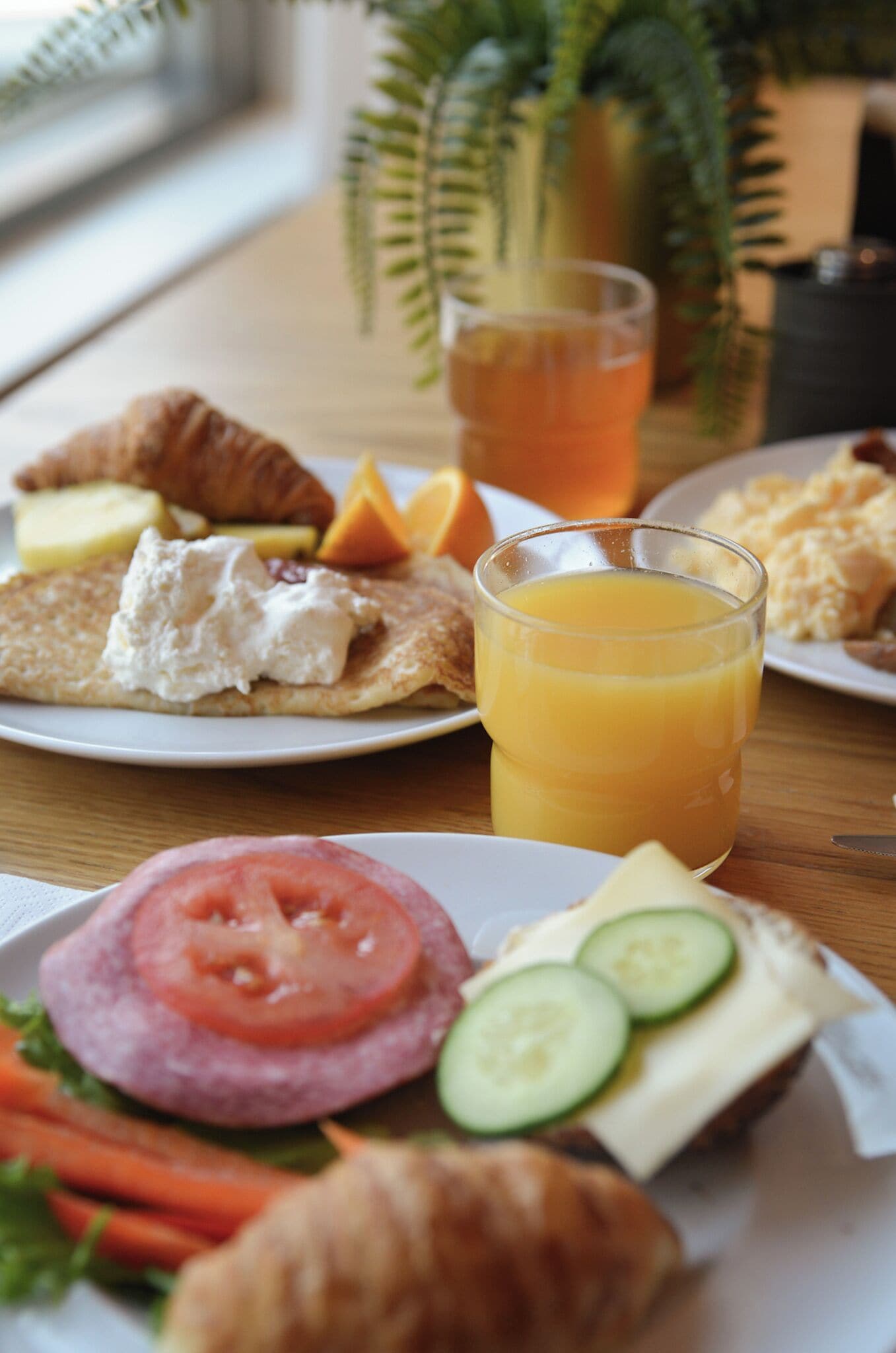 A breakfast setting with croissants, a sandwich, and a glass of orange juice on a wooden table.
