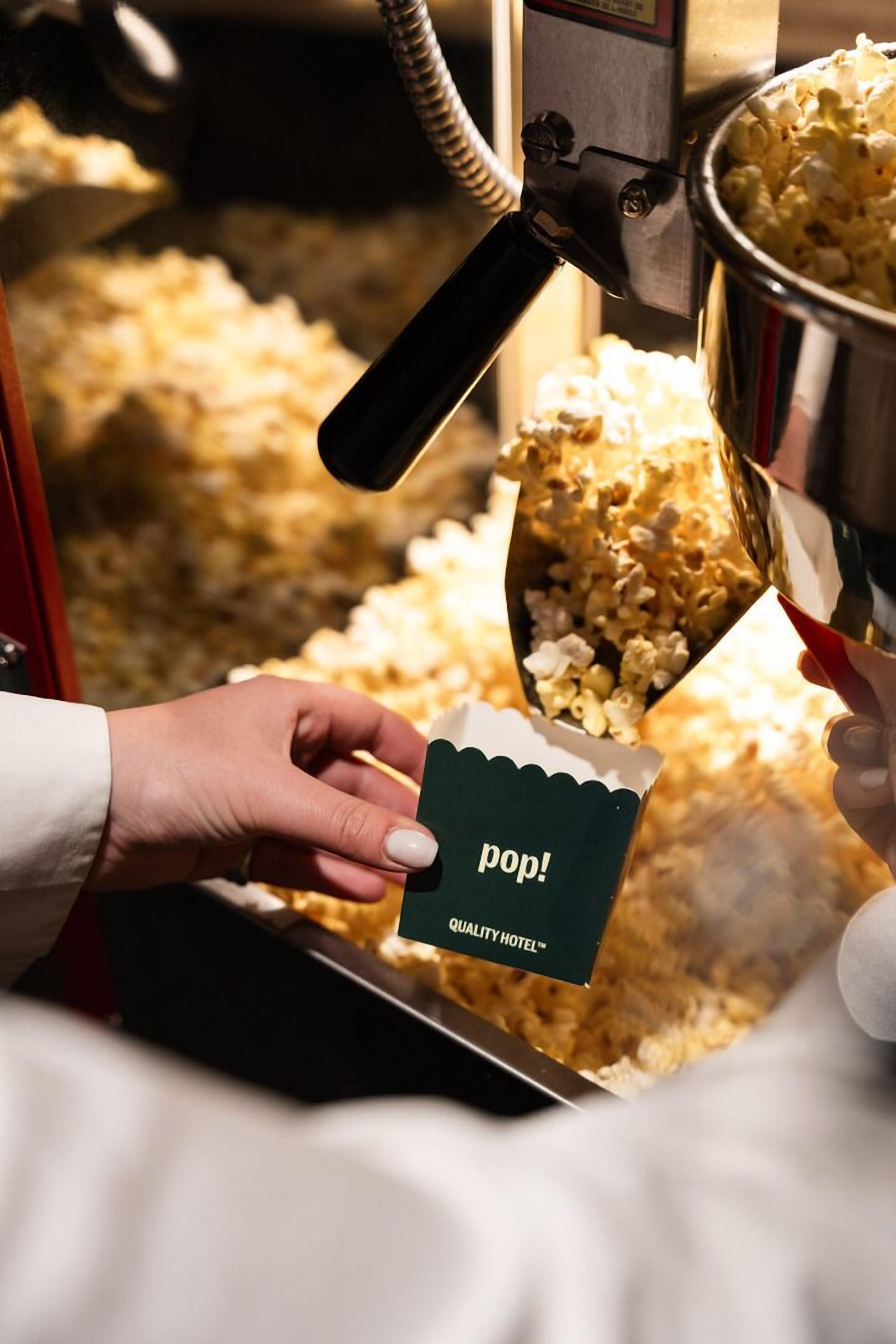 A hand holding a popcorn container with a label, being filled by a popcorn machine.
