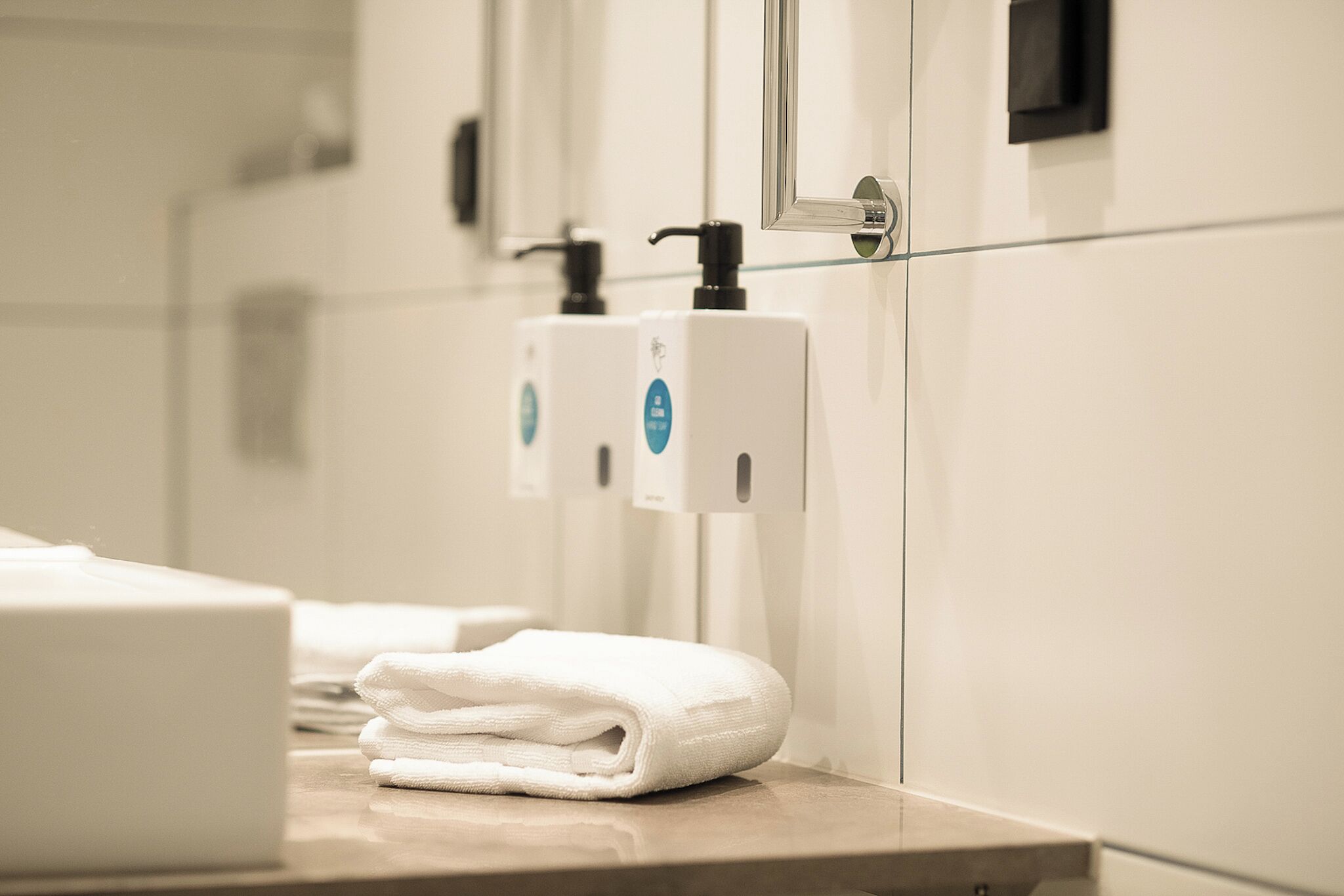Un bagno con erogatore di asciugamani, uno specchio e un divisorio in vetro.
