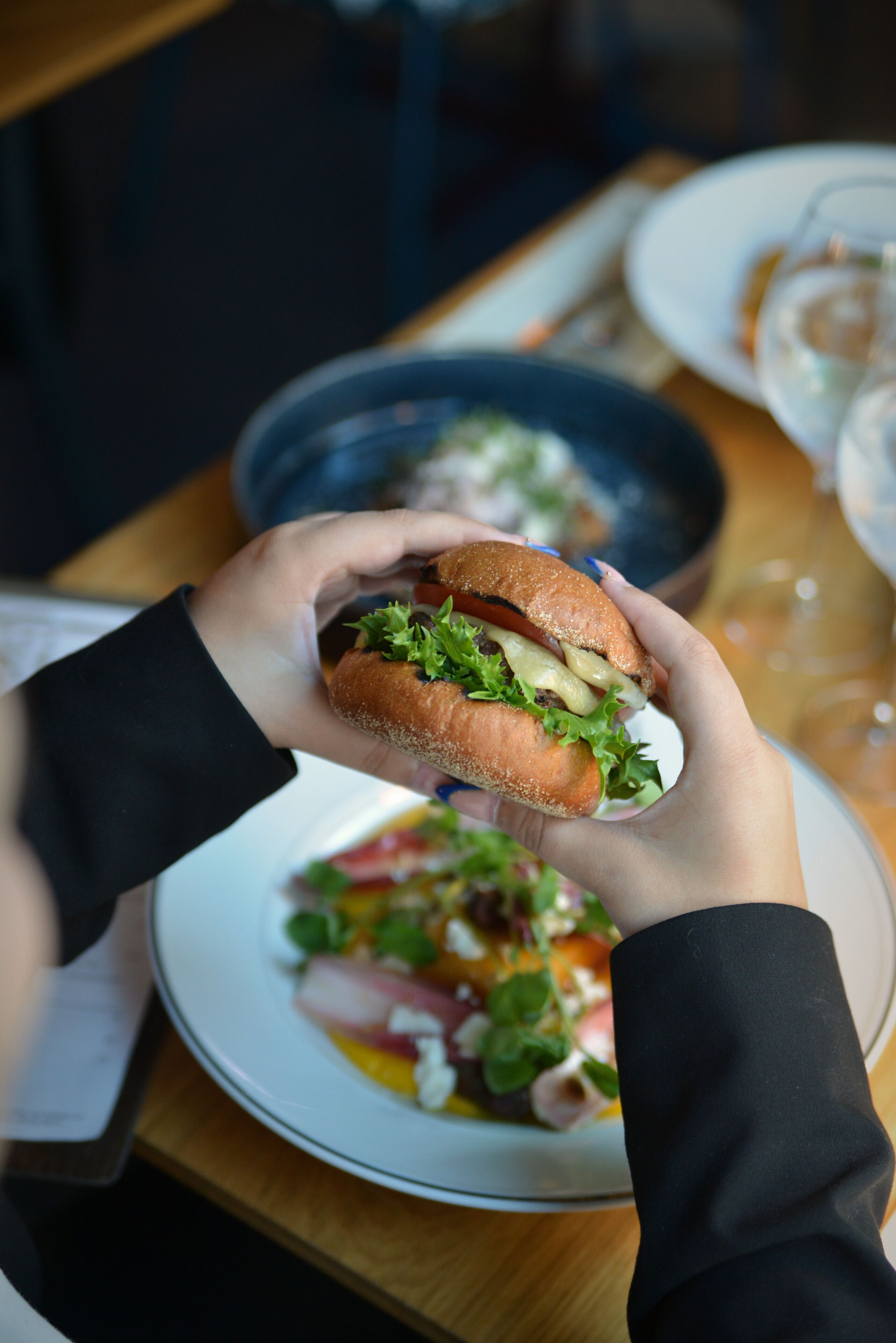 Una persona sosteniendo un sándwich con lechuga y queso visibles.