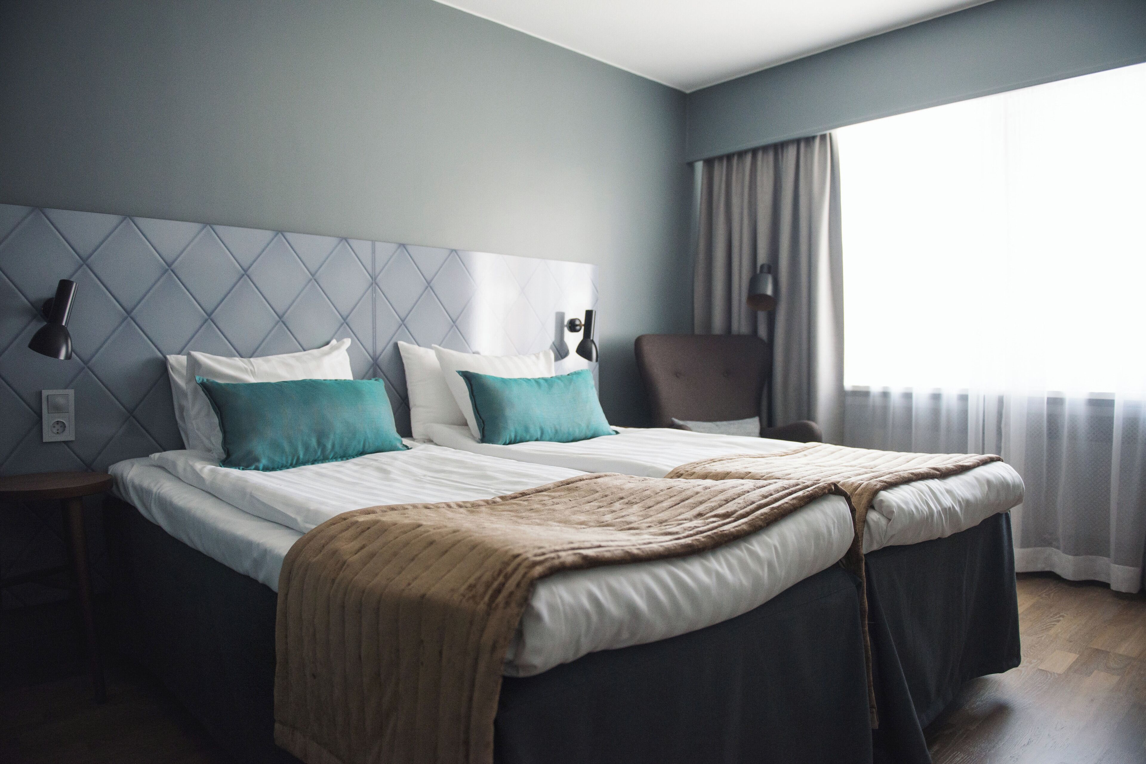 A hotel room with a large bed, two bedside tables, a chair, and a window with curtains.
