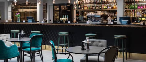A bar area with multiple seating options, including round tables and chairs, and a variety of bottles and glasses on shelves.