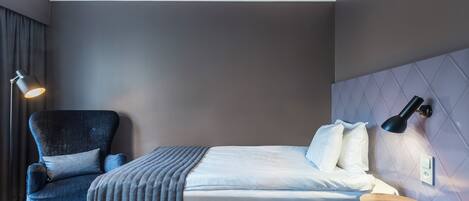 Una habitación de hotel moderna con una cama, una silla, un taburete y una lámpara de pared.