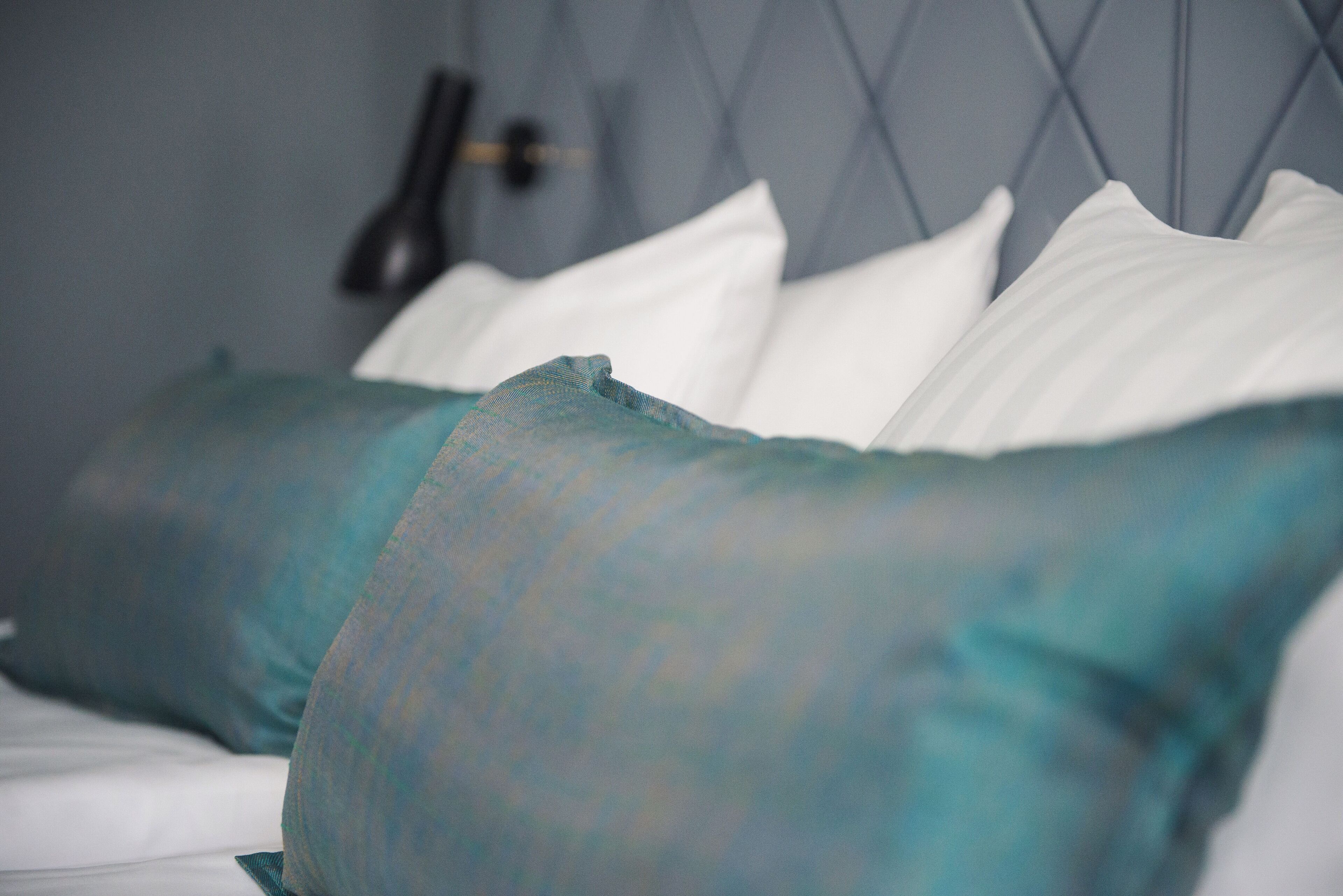 A bed with white and teal pillows, a headboard with a diamond pattern, and a black object on the wall.