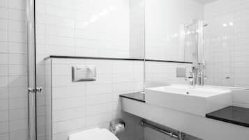 Un baño moderno con azulejos blancos, cabina de ducha de vidrio, inodoro blanco y lavamanos con encimera negra.
