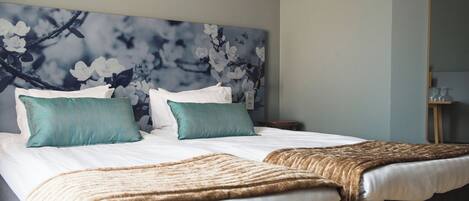 Habitación de hotel con una cama grande, dos almohadas, cabecera con diseño floral y mesita de noche con lámpara.