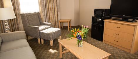 Habitación de hotel con sofá, sillón, una mesita con un florero, televisor, microondas y un mueble de madera.