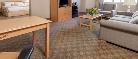 Una habitación de hotel con cama, escritorio, televisor, mesa de centro, sofá y una silla.
