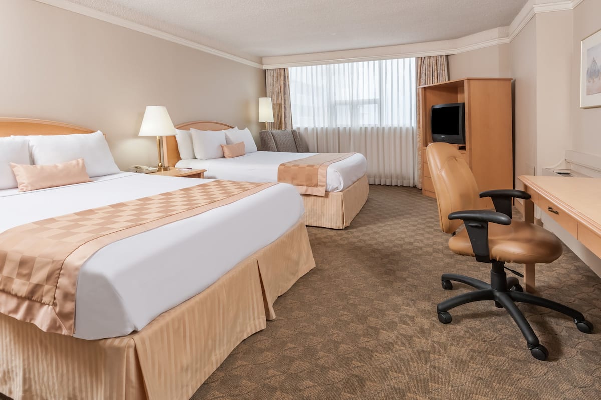 A hotel room with two beds, a desk, a chair, a television, and a wardrobe.