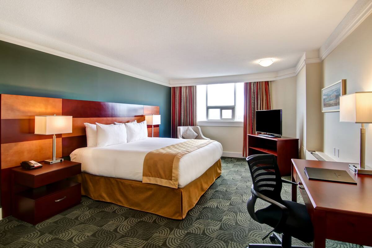 A hotel room with a large bed, a desk, a chair, a TV, and a window with curtains.