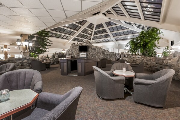 A spacious indoor area with a high ceiling and skylights, featuring comfortable seating and a stone wall with a television.