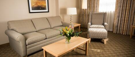 A hotel room with a sofa, armchair, table, lamp, and a framed picture on the wall.