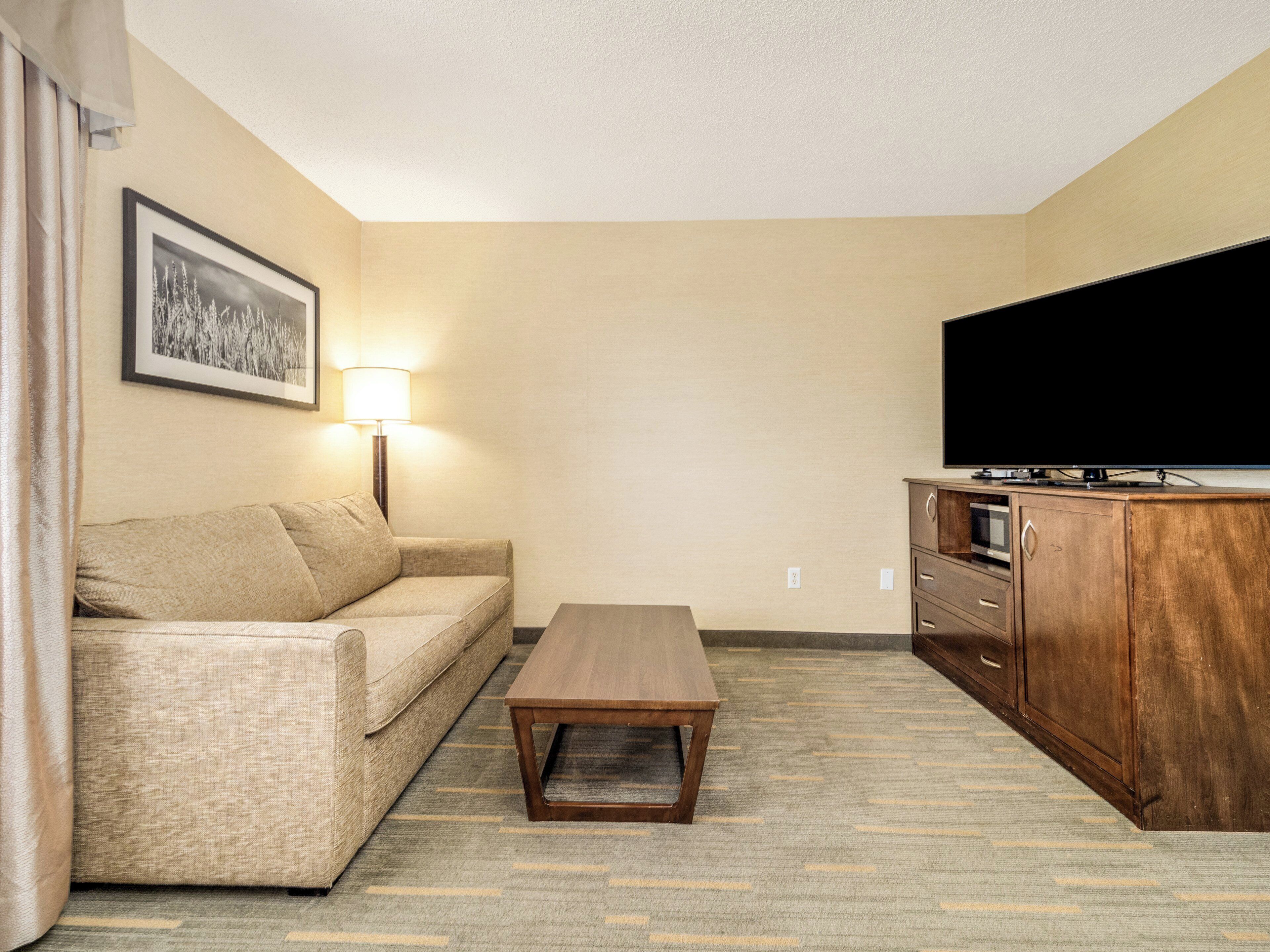 A hotel room with a sofa, a coffee table, a TV, and a wooden cabinet.