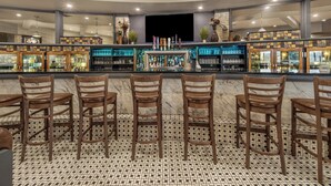 A bar area with a marble floor, wooden chairs, and a counter with various bottles and glasses. - Holiday Inn Lethbridge by IHG (Lethbridge)