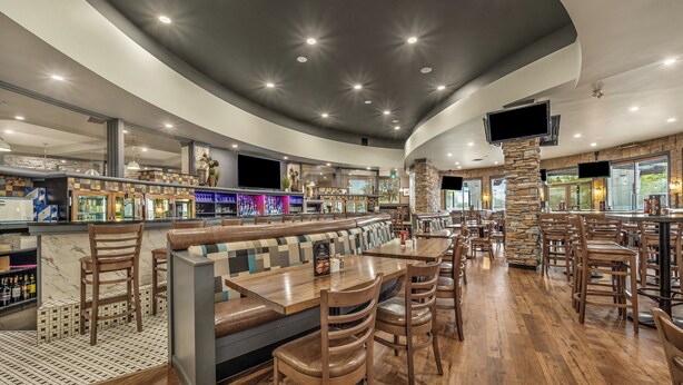 A restaurant with a bar area, wooden tables and chairs, and a stone accent wall. - Holiday Inn Lethbridge by IHG (Lethbridge)