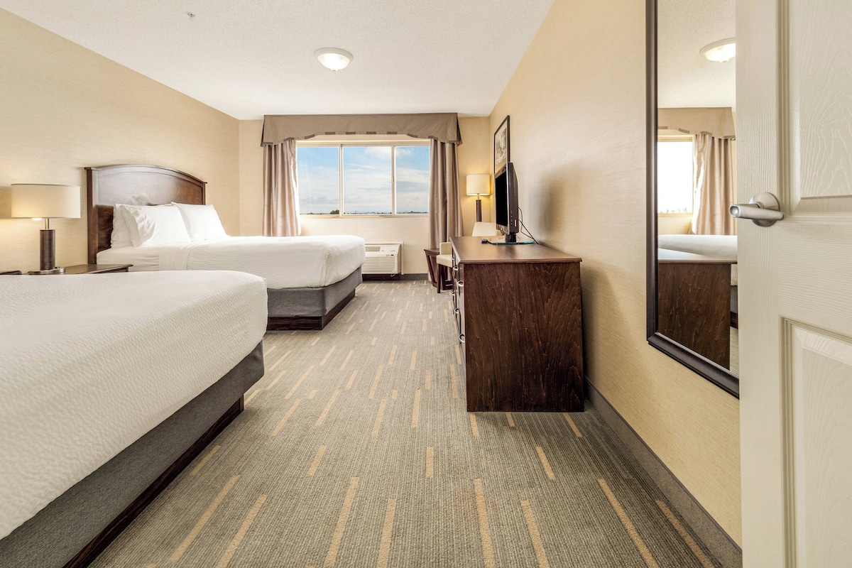 A hotel room with two beds, a desk, a chair, a TV, and a large mirror.