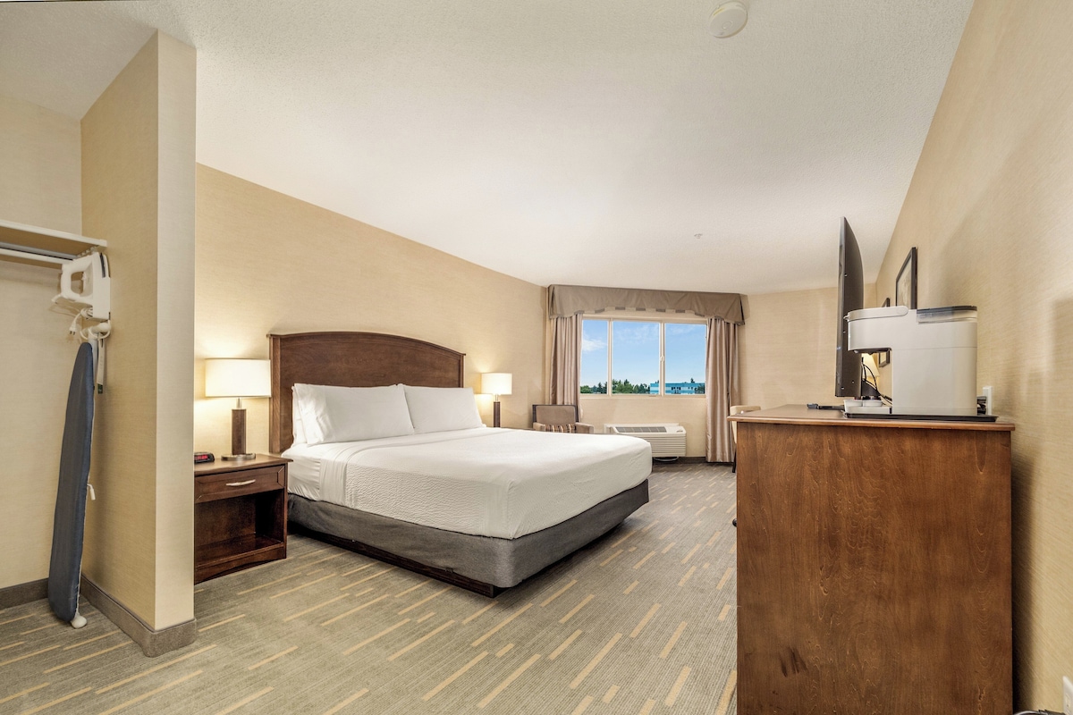 A hotel room with a large bed, bedside lamps, a desk with a computer, and a window with a view.