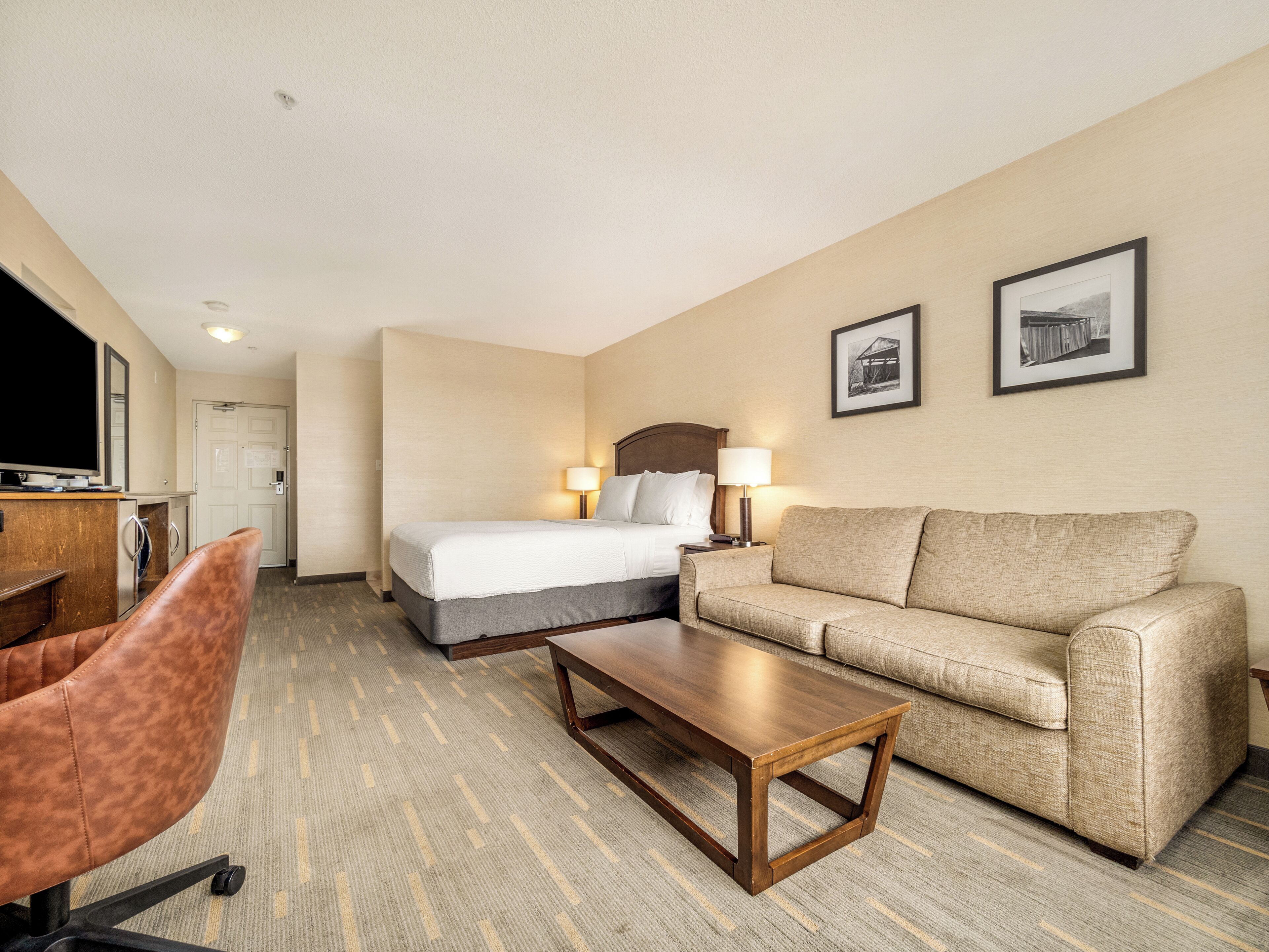 A hotel room with a bed, a sofa, a desk, and a chair.