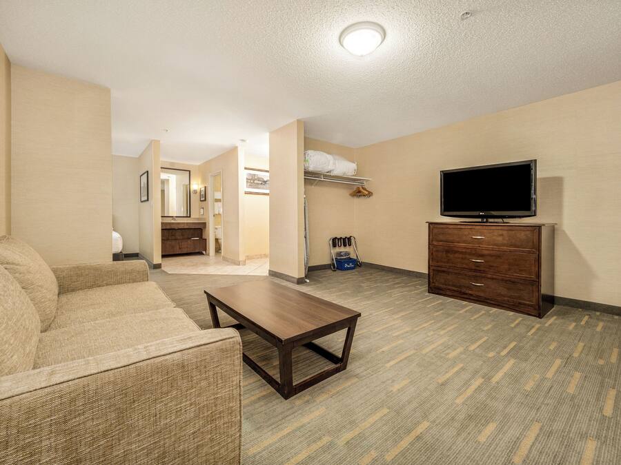 Habitación de hotel con sofá, televisión, cómoda y baño a la vista.
