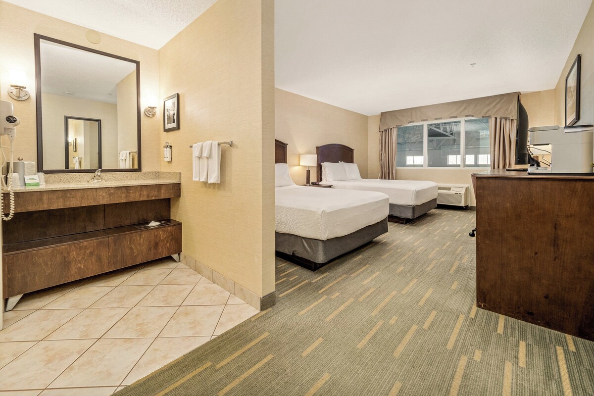 A hotel room with a bathroom, two beds, a desk, and a large mirror.
