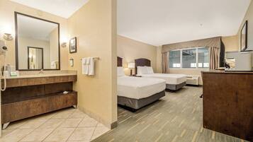 A hotel room with a bathroom, two beds, a desk, and a large mirror.