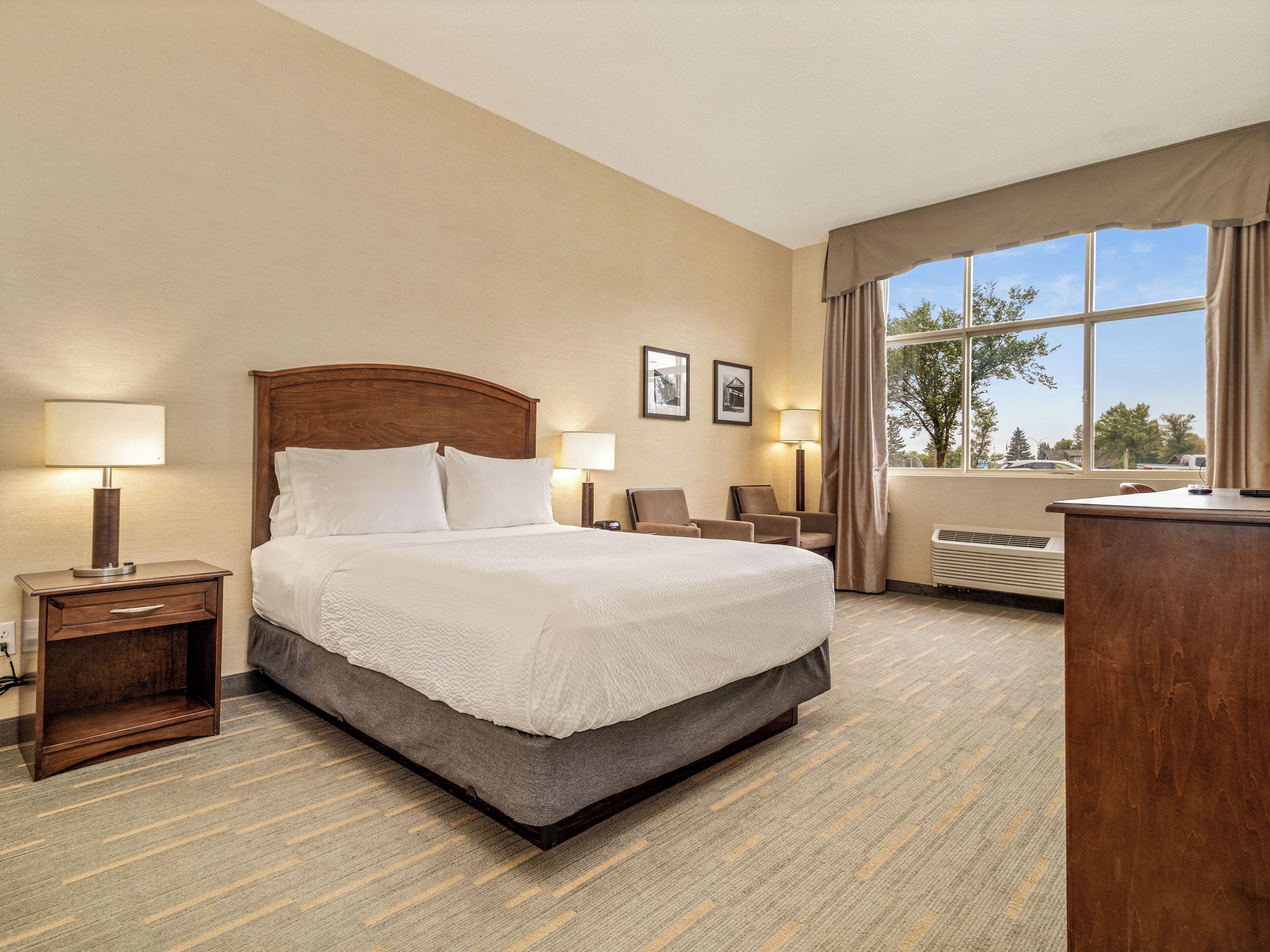 Habitación de hotel con una cama grande, dos mesitas de noche con lámparas, un escritorio y una ventana con cortinas.