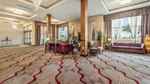 A spacious lobby with a patterned carpet, a reception desk, seating areas, and large windows with curtains. - Holiday Inn Lethbridge by IHG (Lethbridge)