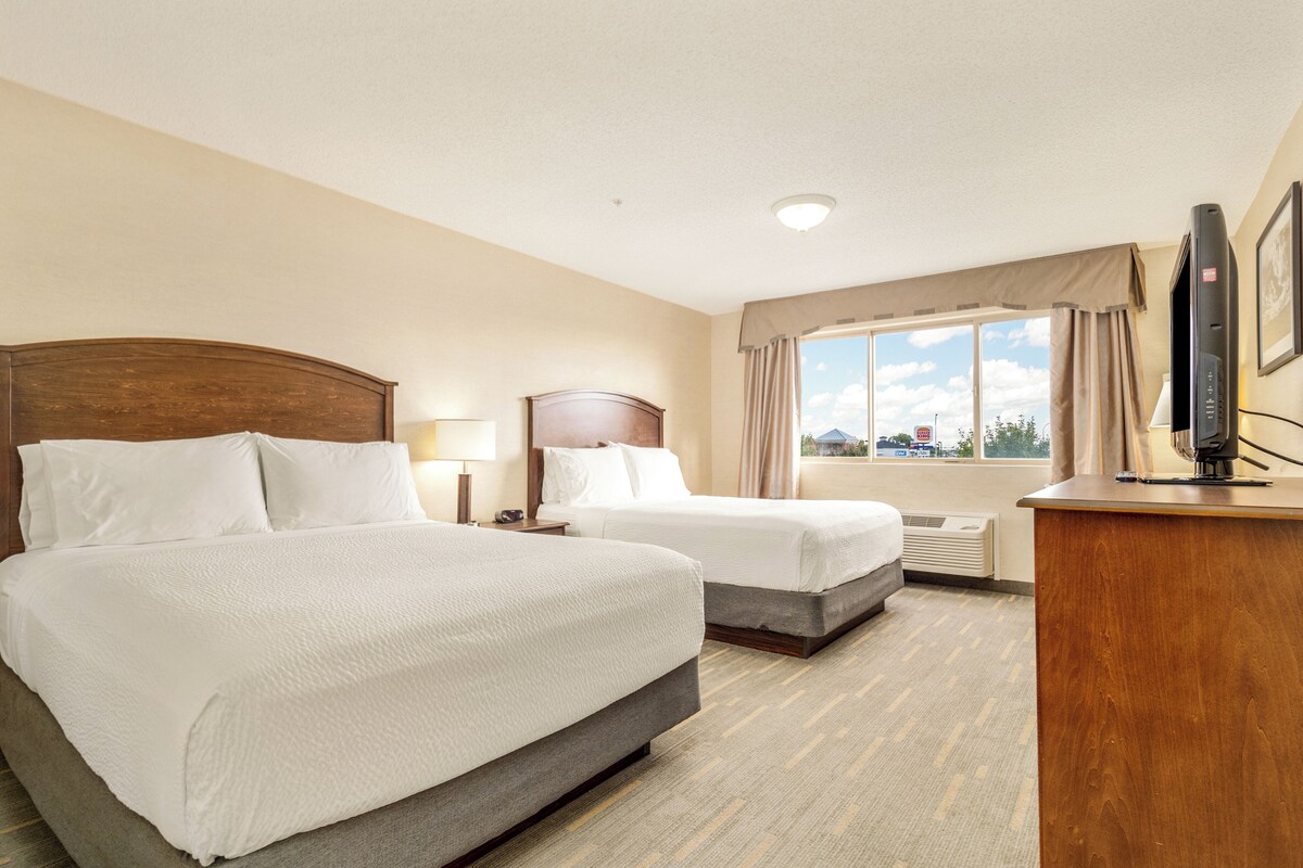 A hotel room with two beds, a desk with a television, and a window with curtains.