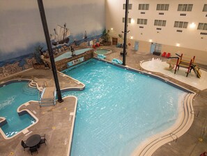 An indoor swimming pool with multiple lanes, a children's play area, and a mural depicting a shipwreck.