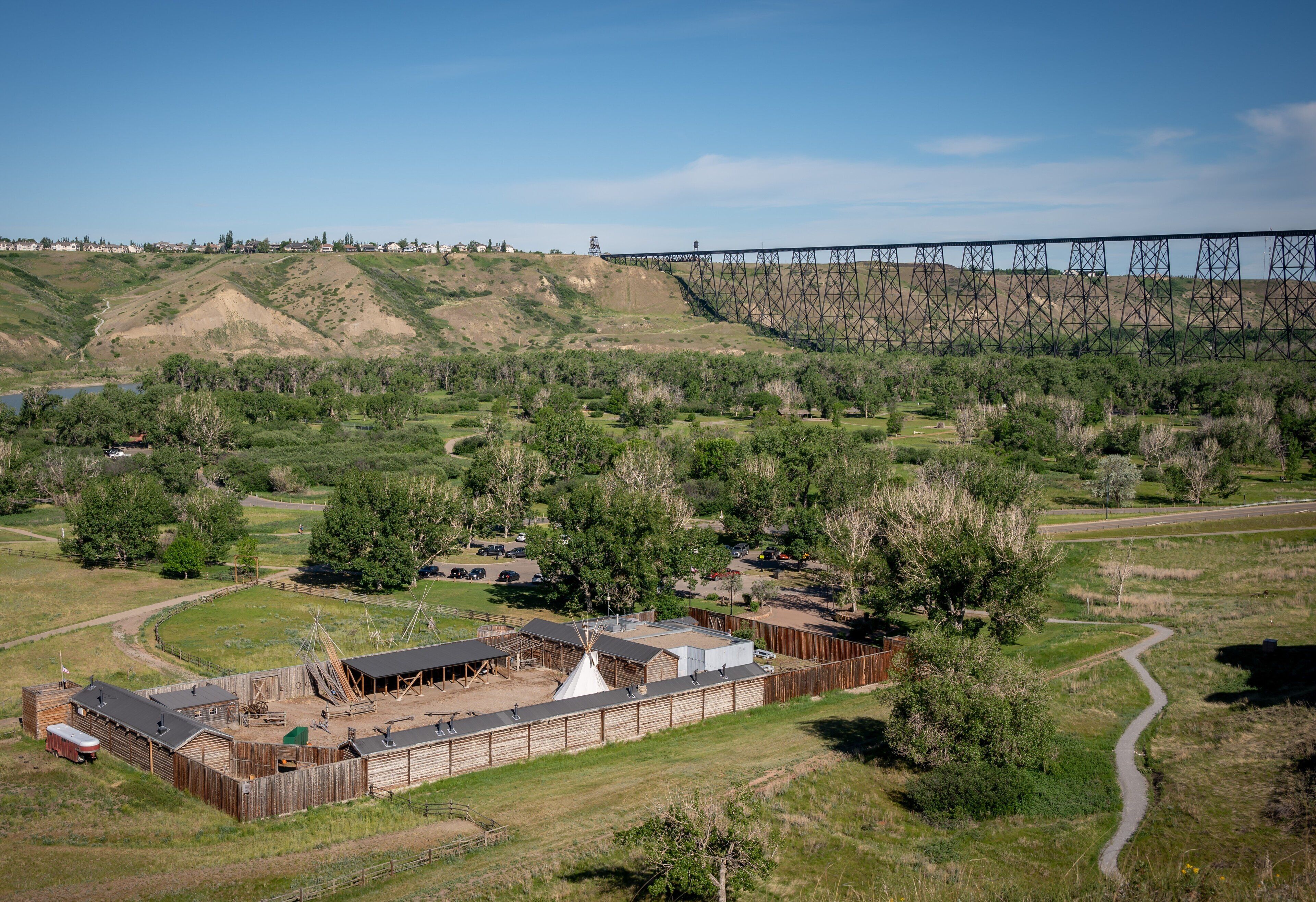 A fenced area with a building, a dirt path, and a bridge in the background.