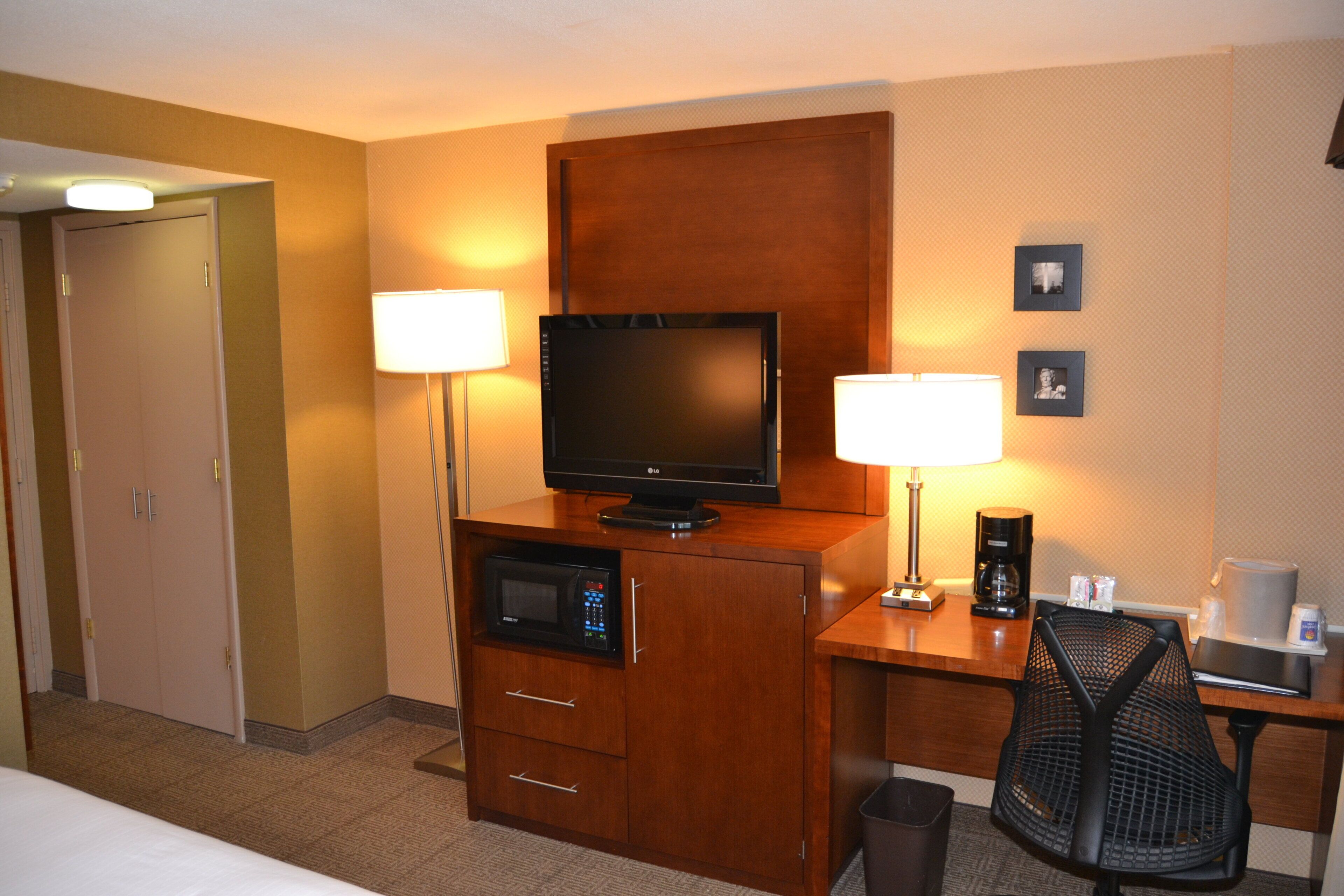 A hotel room with a bed, a desk with a television, a coffee maker, and two lamps.
