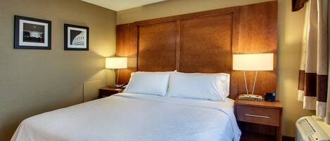 A hotel room with a large bed, two bedside tables with lamps, a wall-mounted heater, and two framed pictures on the wall.