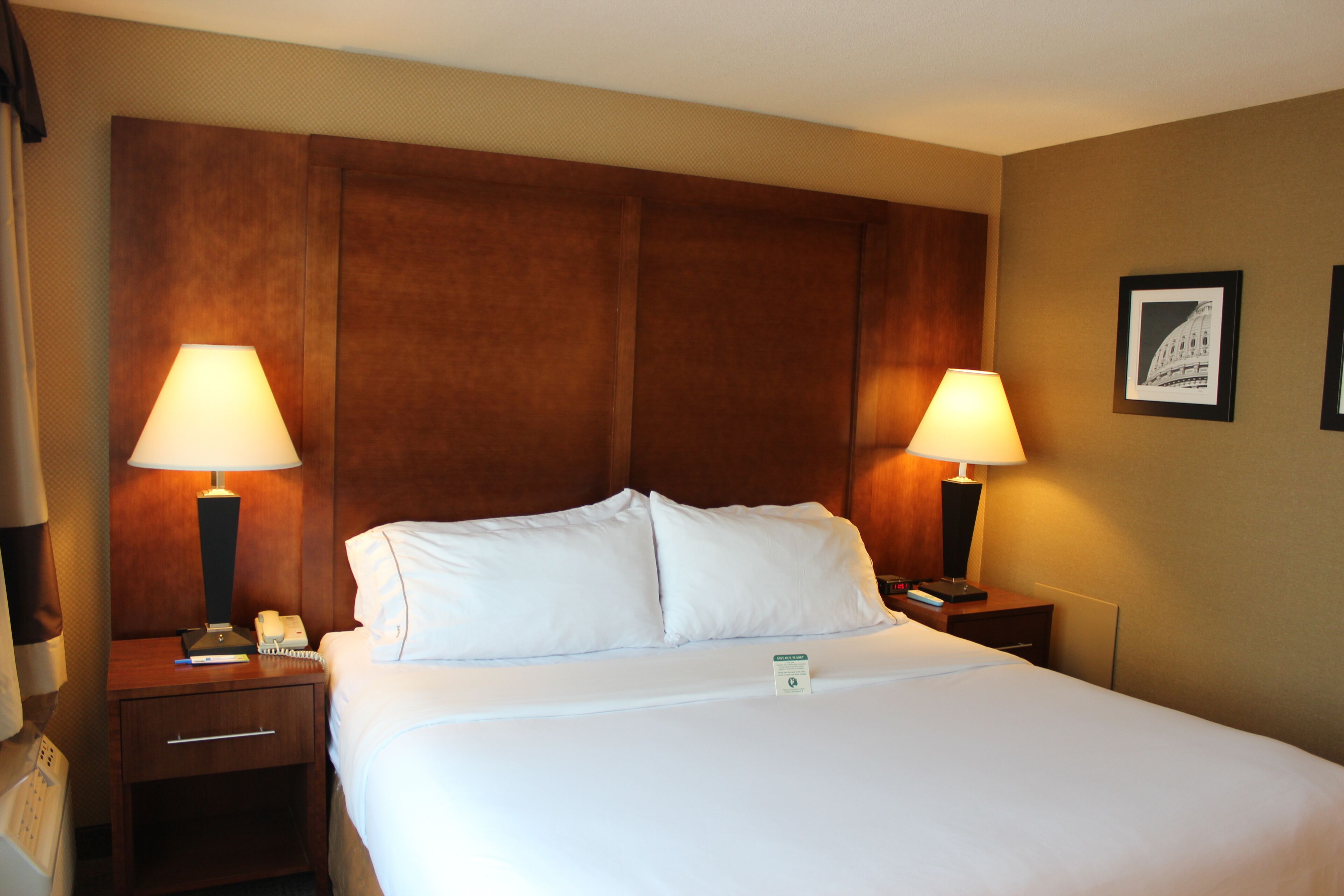 A hotel room with a large bed, two bedside lamps, a nightstand with a phone, and a framed picture on the wall.