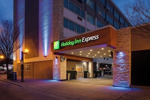 Exterior de un hotel Holiday Inn Express con un diseño moderno, destacando una entrada prominente y señalización iluminada.