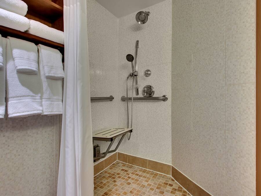 Zona de ducha con cabezal de ducha de mano, grifo empotrado en la pared y estante con artículos de aseo.