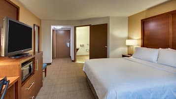A hotel room with a bed, a TV, a desk with drawers, and a bathroom visible through an open door.