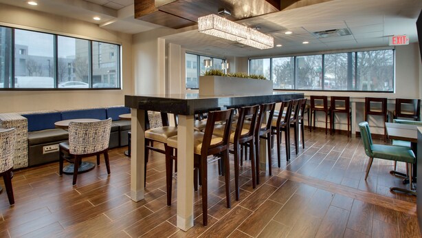 A spacious restaurant with a long counter, multiple seating areas, and large windows offering views of the outside. - Holiday Inn Express Washington DC N-Silver Spring by IHG (Silver Spring)