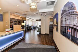 Vestíbulo de hotel con mostrador de recepción, un mural grande en la pared y una zona de estar con mesas y sillas.