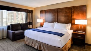 A hotel room with a large bed, a sofa, two bedside lamps, and a view of buildings through the window. - Holiday Inn Express Washington DC N-Silver Spring by IHG (Silver Spring)