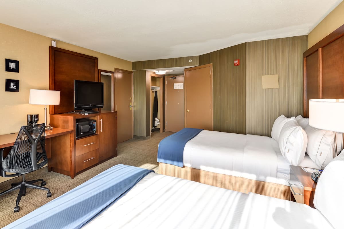 A hotel room with two beds, a desk with a computer, a TV, and a microwave.
