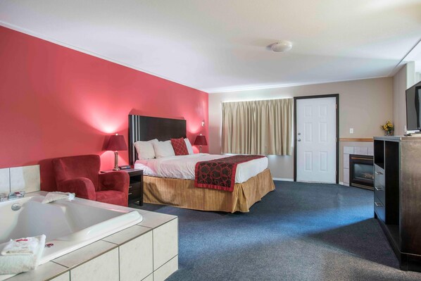 Habitación de hotel con cama, un sillón rojo, escritorio, televisor, chimenea y baño con bañera.