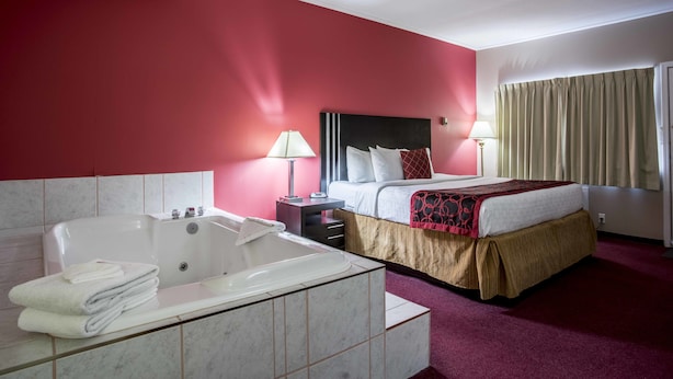 Quarto de hotel com uma cama grande, banheiro separado com banheira e uma parede de destaque vermelha.