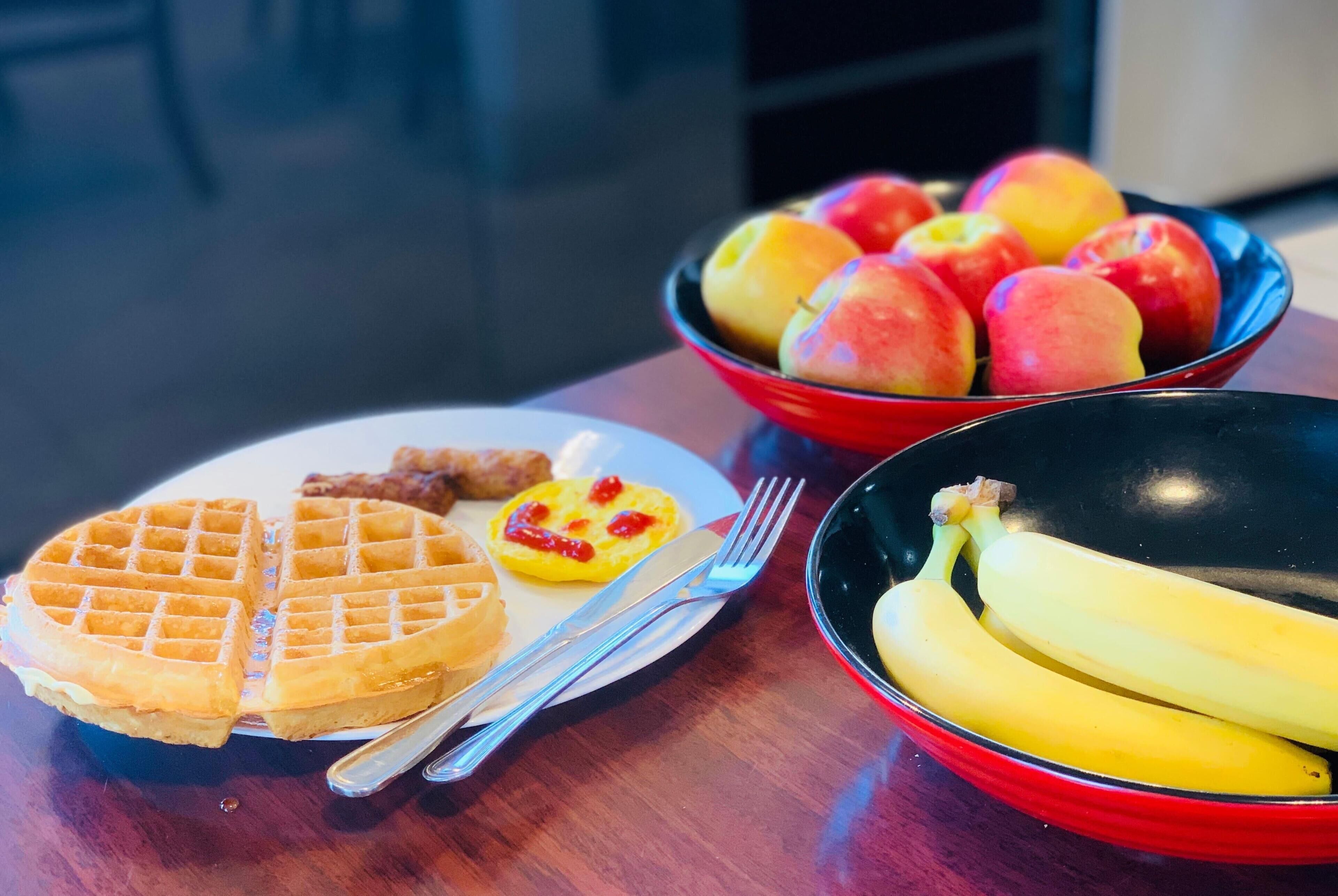 Un plato de desayuno con waffles, un tazón de fruta y un tazón de plátanos.