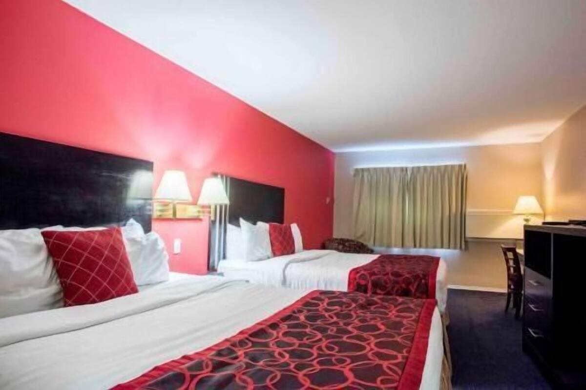 Ein Hotelzimmer mit zwei Betten, einem Schreibtisch, einem Stuhl und einem Fenster mit Vorhängen.