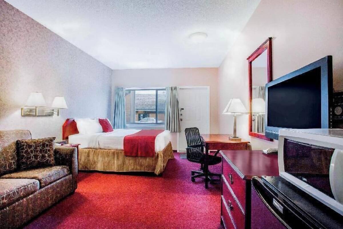 Ein Hotelzimmer mit Bett, Schreibtisch, Fernseher, Sessel und Fenster.