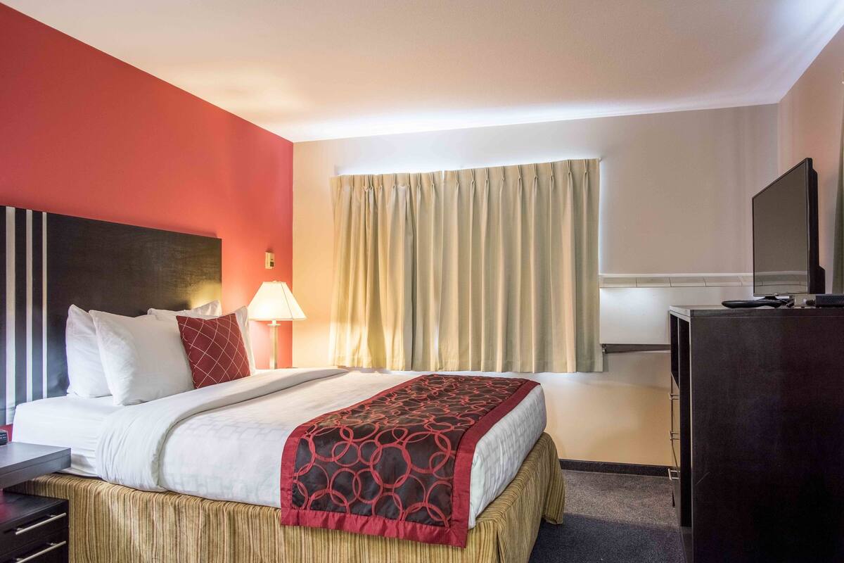 Ein Hotelzimmer mit einem Bett, einem Schreibtisch, einem Fernseher und einem Vorhangfenster.