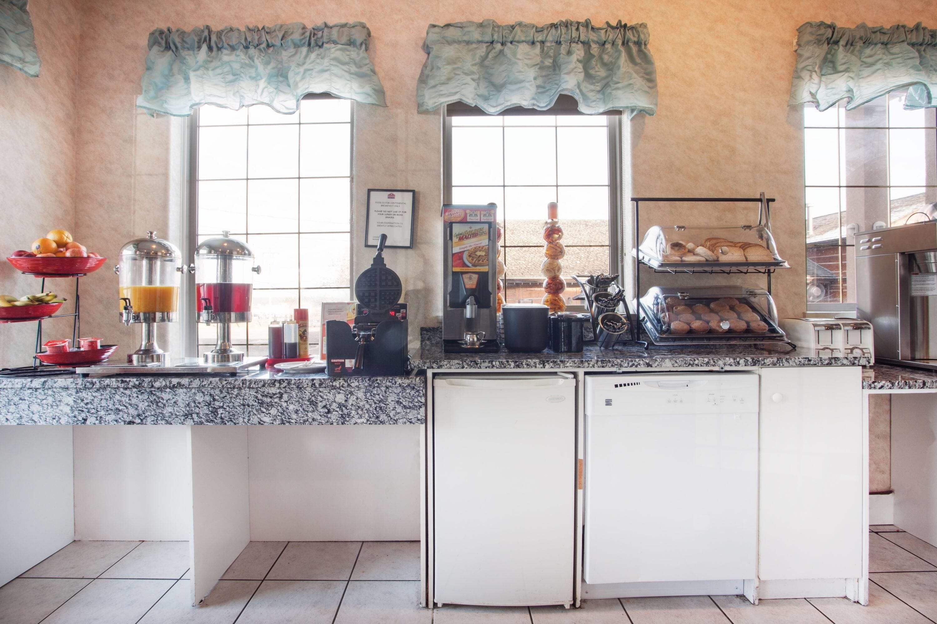 A kitchen with a granite countertop, a coffee machine, a waffle maker, and a bread display.